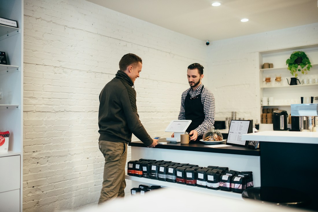 A shop owner talking with a customer across the counter of a small café.